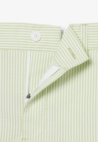 Groen-wit gestreepte broek met een open ritssluiting, een witte knoop aan de tailleband en een klittenbandsluiting onder de flap.