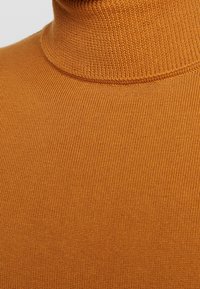 Suéter de cuello alto en un cálido tono naranja, con textura acanalada y diseño ceñido. Tejido suave con cuello sin costuras.
