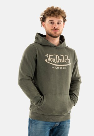 Un sweat à capuche vert avec une poche kangourou à l'avant, arborant un imprimé crème. Tissu doux avec une coupe décontractée, associé à un jean bleu.