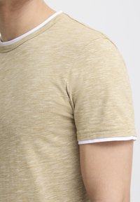 Tricou scurt cu mânecă scurtă, de culoare bej deschis, cu o textură heathered, având un guler alb tip crew și cusături curate pe mâneci.
