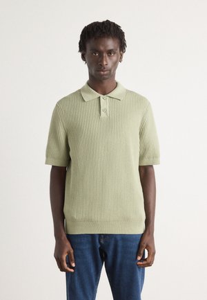 Strikket polo skjorte i lysegrønn med korte ermer, ribbet tekstur og tre-knapps knappestolpe. Kombinert med mørkeblå denimjeans.