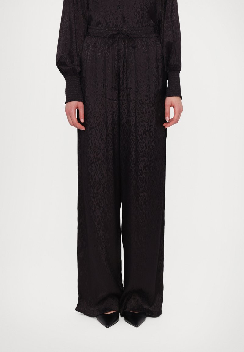 Svart mønstrete jumpsuit med snøring i midjen, knappestolpe foran og lange ermer. Laget av glatt stoff, med brede, flytende ben.
