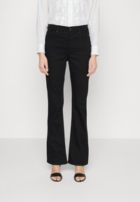 Svarta utsvängda jeans i denim, med en medelhög midja, fem fickor och subtila stickningsdetaljer. Bärs med en vit skjorta.