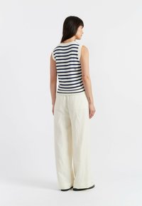 Top a maniche scoperte, a righe navy e bianche in maglia, con orlo a coste, abbinato a pantaloni larghi color crema realizzati in tessuto leggero.