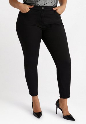 Jeans ajustados negros de cintura alta, con bolsillos frontales, un dobladillo ligeramente deshilachado, combinados con tacones negros puntiagudos y una blusa de lunares.