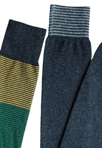 Due paia di calzini; quello sinistro presenta strisce verdi e gialle; quello destro è di un grigio scuro uniforme con un polsino a costine. Entrambi hanno una finitura a maglia testurizzata.