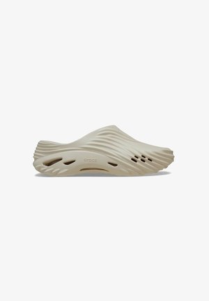 Beige crocs with a wavy design, made of lightweight material. Features side ventilation holes and a streamlined silhouette.