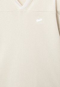 Witte mesh v-hals top met een subtiele textuur en kleine perforaties, geaccentueerd door een wit logo aan de voorkant.