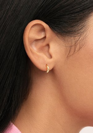 Pendiente de aro dorado con un acabado suave, que presenta un diseño curvo minimalista. La superficie brillante refleja la luz, realzando su apariencia elegante.