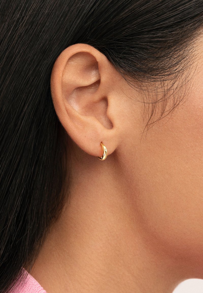 Boucle d'oreille anneau en or avec une finition lisse, présentant un design minimaliste incurvé. Sa surface brillante reflète la lumière, mettant en valeur son apparence élégante.