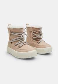 Bottines en faux suède beige avec une doublure blanche duveteuse, des lacets en corde et une fermeture éclair sur le côté, montées sur une semelle plateforme blanche texturée.