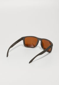 Gafas de sol de madera con un acabado de veta oscura y lentes de color ámbar, con un marco cuadrado y brazos delgados.