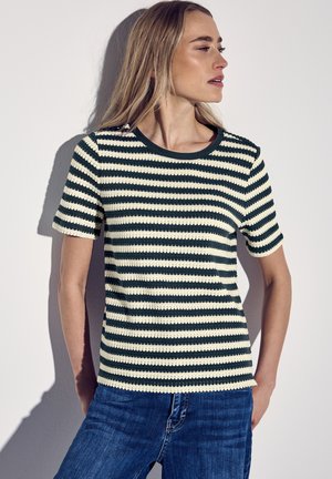 Striped knit short-sleeve top in dark green and cream, featuring a rounded neckline and textured fabric. Paired with blue denim jeans.