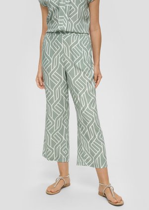 Lichtgroene, gepatteerde broek met vloeiende wijde pijpen, featuring een abstract wit ontwerp. Gecombineerd met platte, gespsandalen.