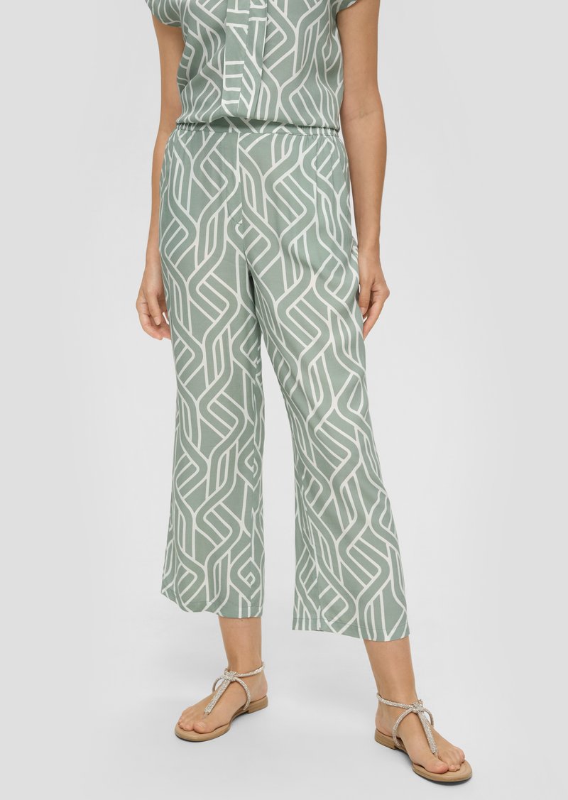 Lichtgroene, gepatteerde broek met vloeiende wijde pijpen, featuring een abstract wit ontwerp. Gecombineerd met platte, gespsandalen.
