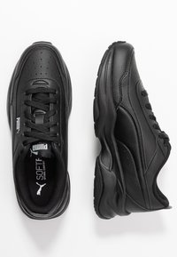 Chaussures de sport noires en cuir synthétique. Les caractéristiques incluent des détails perforés, des lacets, un col rembourré et une semelle rembourrée.