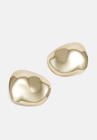 Boucles d'oreilles en métal doré avec une surface lisse et réfléchissante, ayant une forme de galet organique, avec des bords arrondis et une finition poli.