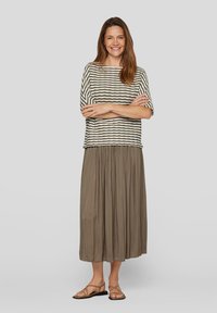 Striped shirt in beige and dark olive, paired with a long, pleated khaki skirt. Sandals with crisscross straps and a smooth finish.