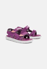 Violetti sandaalit säilyttävillä säädettävillä hihnoilla, rakenteellisella pohjalla ja valkoisella kumipohjalla. Sisältää Timberland-logon ja kontrastiväriset vaaleanpunaiset yksityiskohdat.