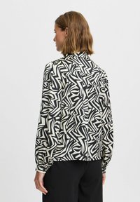 Blusa a maniche lunghe con un motivo astratto a zigzag in nero e crema. Presenta un colletto e polsini arricciati, realizzata in un tessuto leggero.
