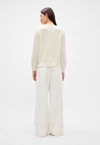 Crème kleurige gebreide trui met lange mouwen en een licht gestructureerde stof. Gepaarde met hoge taille, wijdvallende, witte broek met achterzakken.