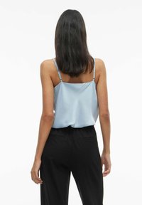 Svijetloplava satenasta majica s tankim naramenicama, sa opuštenim krojem i glatkom teksturom, u kombinaciji s crnim hlačama visokog struka.