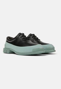 Scarpe di pelle nera con suola in gomma verde menta, caratterizzate da una forma arrotondata, design con lacci e dettagli texturizzati lungo la suola.