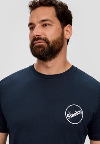 Granatowa bawełniana koszulka z okrągłym białym logo na piersi z napisem „Sinalco”. Posiada klasyczny okrągły dekolt oraz krótkie rękawy.