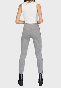 Leggings grises de canalé con franjas laterales negras, diseño de cintura alta, silueta ajustada, combinados con una blusa sin mangas blanca y botas de tobillo de tacón.