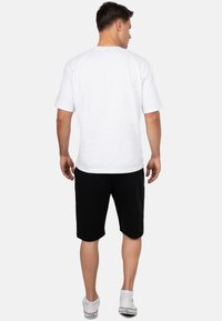 T-shirt blanc à manches courtes avec une coupe droite, associé à un short de sport noir. Le modèle porte des baskets blanches avec des accents noirs.