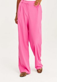 Jasnoróżowe spodnie szerokie, wykonane z gładkiego materiału, z zakładkami z przodu i zestawione z butami w leopardzi wzór.