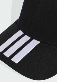 Gorra de béisbol negra con una corona redondeada, que presenta tres franjas bordadas en blanco en la visera. El material muestra un detalle de tejido texturizado.