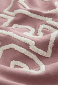 Roosa kangas tekstuurse valge joonistusega geomeetrilises mustris. Pehme, sametine tekstuur, millel on kontrastsed sujuvad alad.