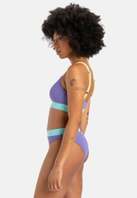 Purple and turquoise ribbed bikini set with adjustable yellow straps. The top features an asymmetrical design, the bottoms have a high-waisted cut.