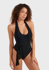 Crni jednodijelni kupać outfit s dubokim izrezom i halter trakama. Ima teksturirani crni pojas na struku. Glatka tkanina.