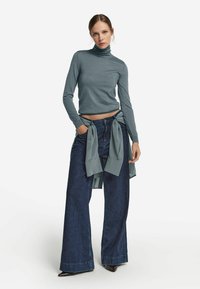 Hellblaue Rollkragenpullover mit langen Ärmeln, kombiniert mit dunklen, weit geschnittenen Jeans. Die Jeans haben eine gebundene Taillenakzent in passendem blauen Stoff.