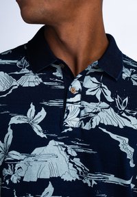 Námořnická polo košile s květinovým a horským potiskem v světle modré barvě. Obsahuje klasický límec a knoflík u výstřihu.