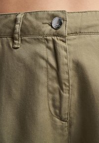 Olivenfargede bomullsshorts med flat front, knappelukking og sidelommer. Glatt tekstur med synlige sømdetaljer.