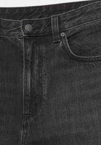 Détail avant d'un jean en denim noir montrant le bouton, la boucle de ceinture, un petit rivet et les coutures de la poche en vue rapprochée.