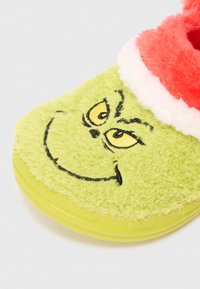Zielona, puszysta klapka o teksturowanej powierzchni, z motywem twarzy Grincha i jasnoczerwoną, futrzastą obrączką. Lekko przezroczysta podeszwa.
