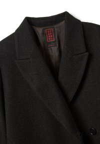 Zwarte wollen jas met notched lapel kraag en zichtbaar rood en zwart merklabel met de tekst "Stefanel Made in Italy."