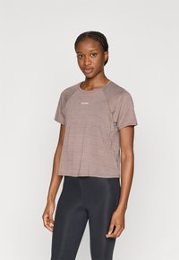 Kortermet sportsgenser i mauve med strukturert finish, rund hals og lett stoff. Har en liten hvit logo på brystet.