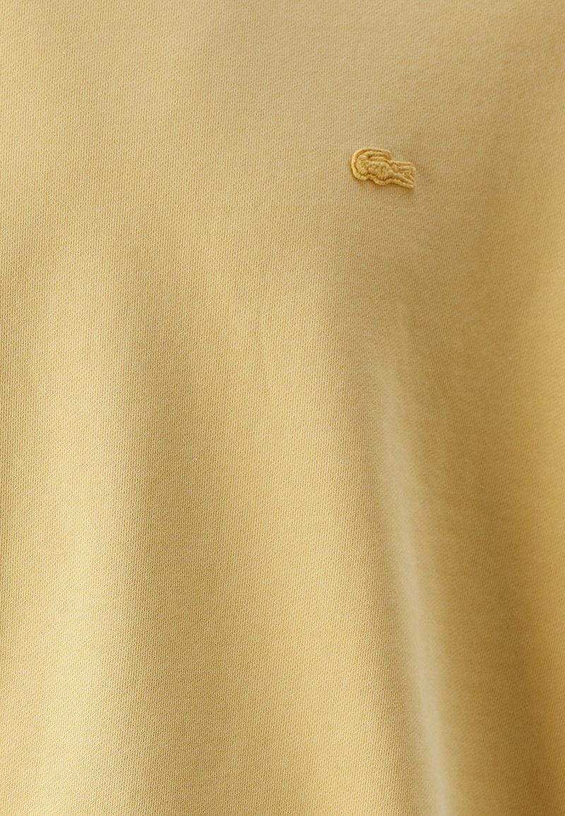 Geel katoenen t-shirt met een gladde textuur, voorzien van een klein geborduurd logo op de borst. Eenvoudige ronde hals en korte mouwen.