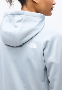 Κοντινό πλάνο ενός ατόμου που φοράει μια ανοιχτό μπλε υφασμάτινη φούτερ με κουκούλα, με το λογότυπο της The North Face στον πίσω ώμο.