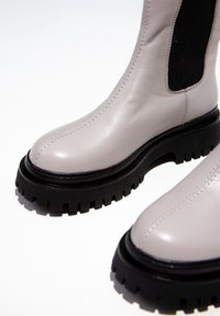 Botines de cuero gris claro con suelas de goma negras, detalles texturizados, paneles laterales elásticos y costuras detalladas a lo largo de las uniones.