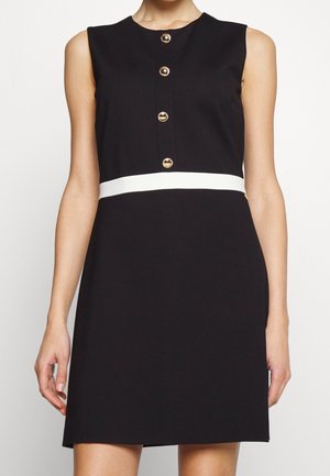 Czarna sukienka bez rękawów z białym, poziomym paskiem na talii oraz czterema złotymi guzikami ułożonymi pionowo na piersi.