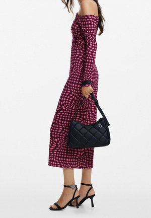 Off-shoulder lyserød ternet kjole med svungne mønstre, tætsiddende design og længde til midt på læggen, parret med en sort quiltet håndtaske og sorte sandaletter.