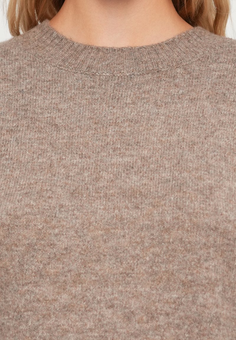 Brązowy sweter z dzianiny z okrągłym dekoltem. Tkanina wydaje się miękka i nieco teksturowana, z subtelnym melanżowym wzorem w całej powierzchni.