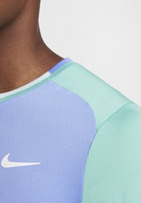 Camiseta deportiva Nike con un diseño de punto de jersey en morado y azul claro, con una textura transpirable y un logo blanco en el pecho.