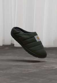 Grøn, polstret slip-on sko med sort gummisål. Har "SUBU" branding og et lille orange logo på siden. Letvægtsdesign.